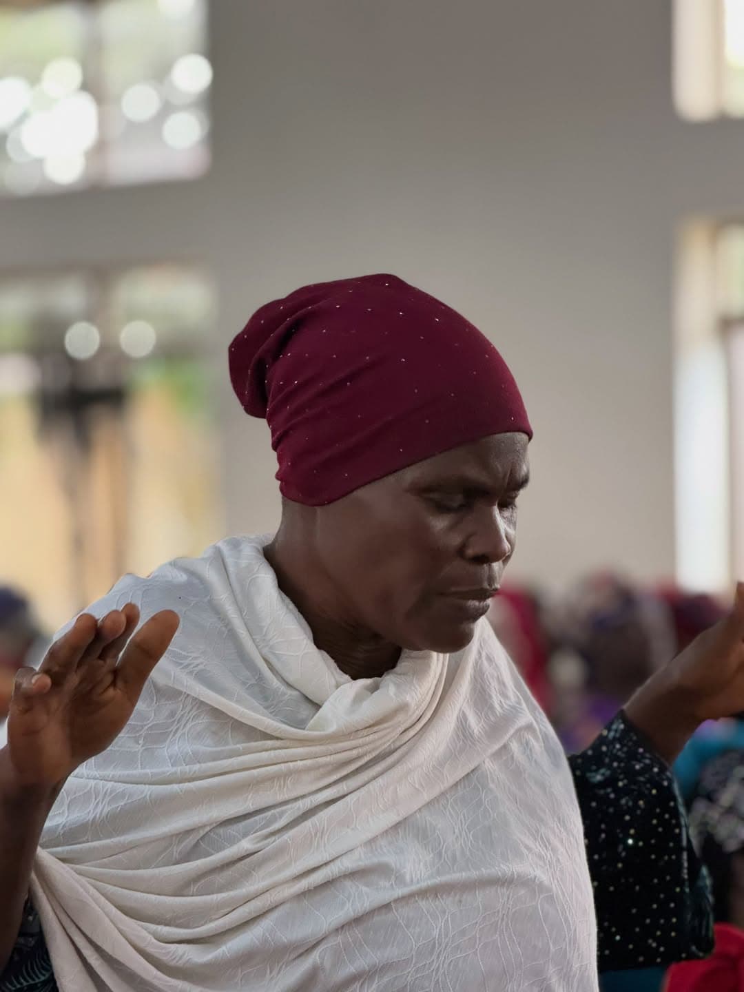 A widow in a headwrap, hands raised in prayer